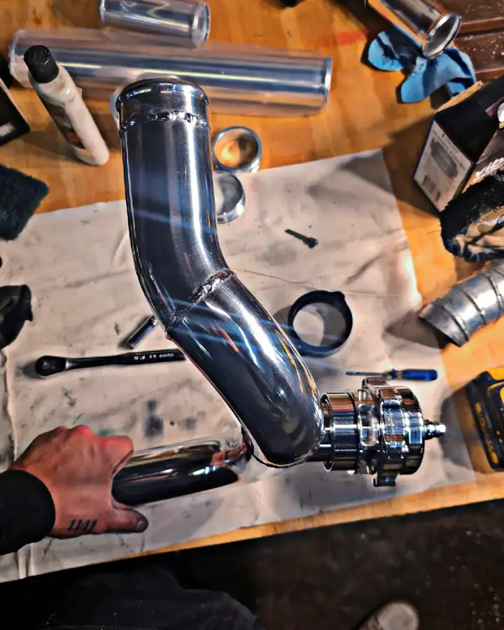 BOV pipe fabrication — A polished charge-pipe section fitted with a blow-off-valve flange.